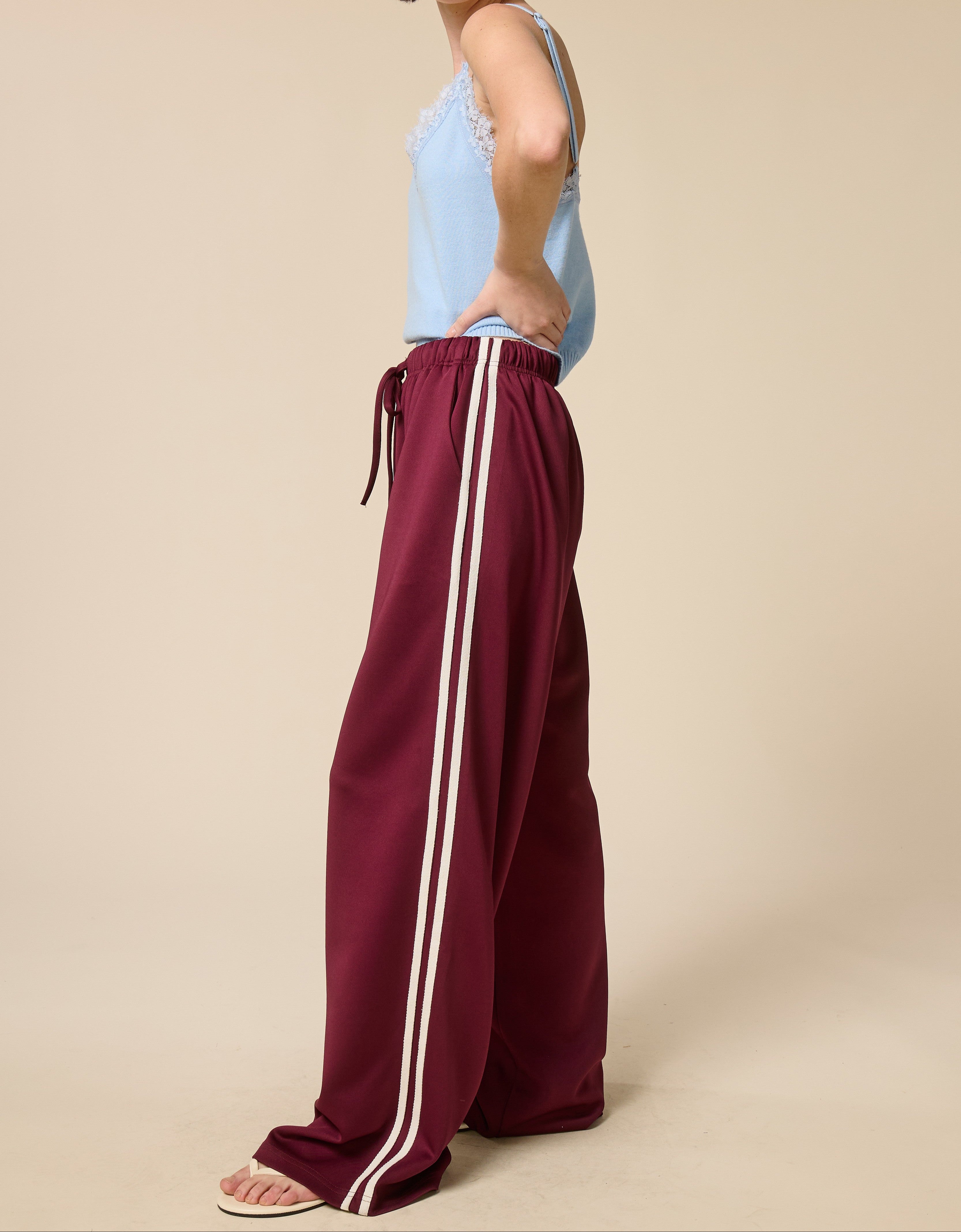 Woman wearing burgundy pants with white stripes and a light blue top on a beige background