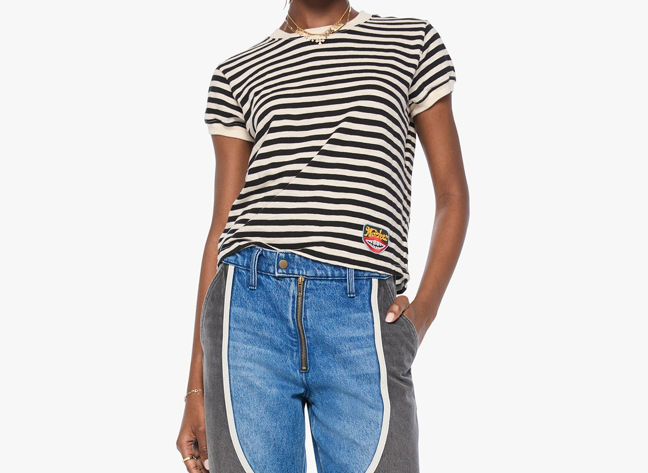 A model wearing a black and white striped t-shirt and distinctive patchwork wide-leg jeans featuring blue denim and dark gray panels separated by white piping, set against a plain white background.