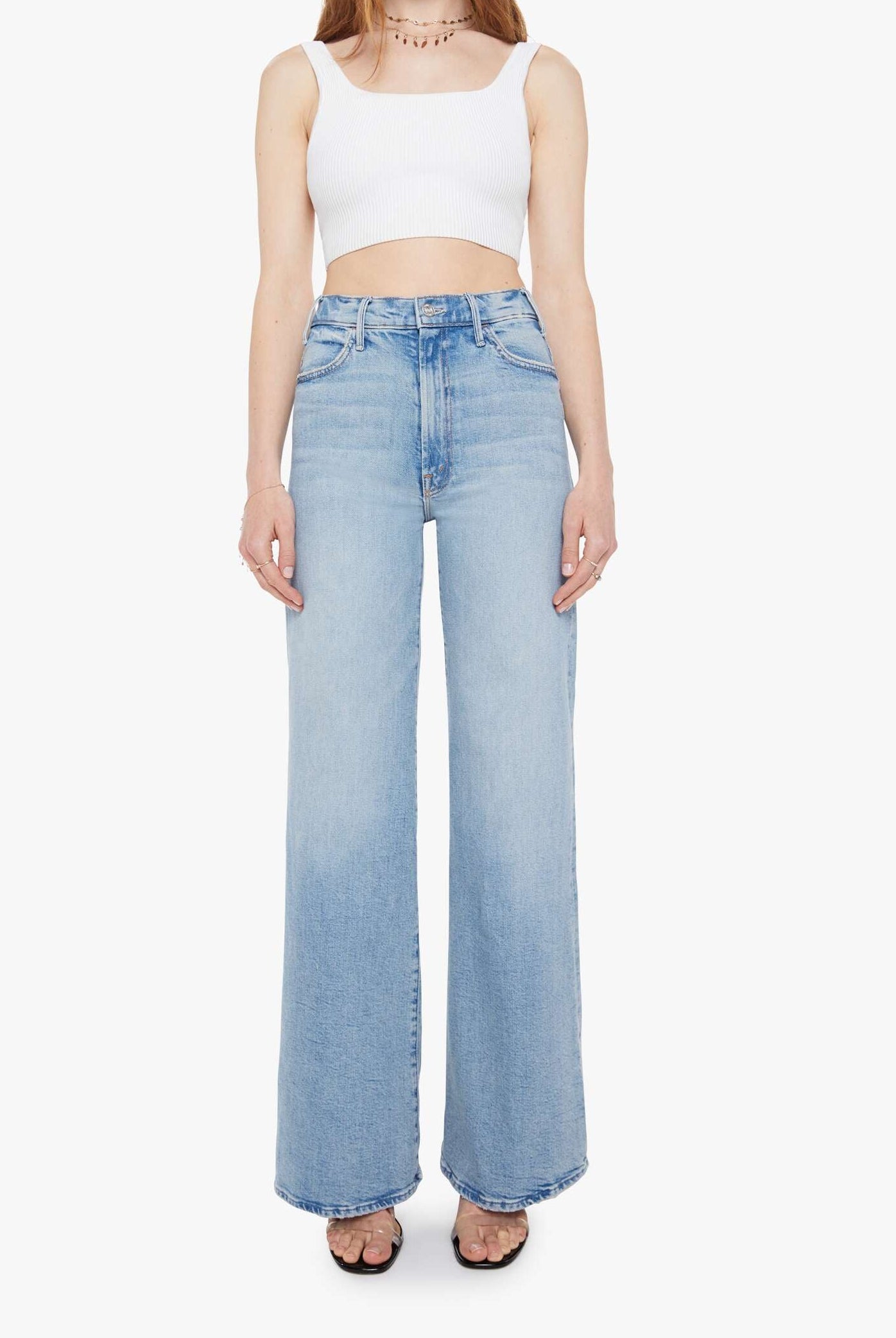 Woman wearing a white sleeveless top and light blue jeans on a white background
