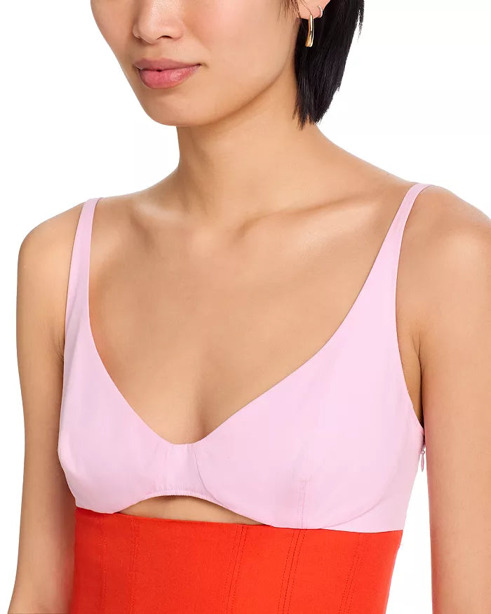 Woman wearing a light pink bralette with a red garment underneath on a white background