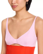 Woman wearing a light pink bralette with a red garment underneath on a white background