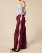 Woman wearing burgundy pants with white stripes and a light blue top on a beige background
