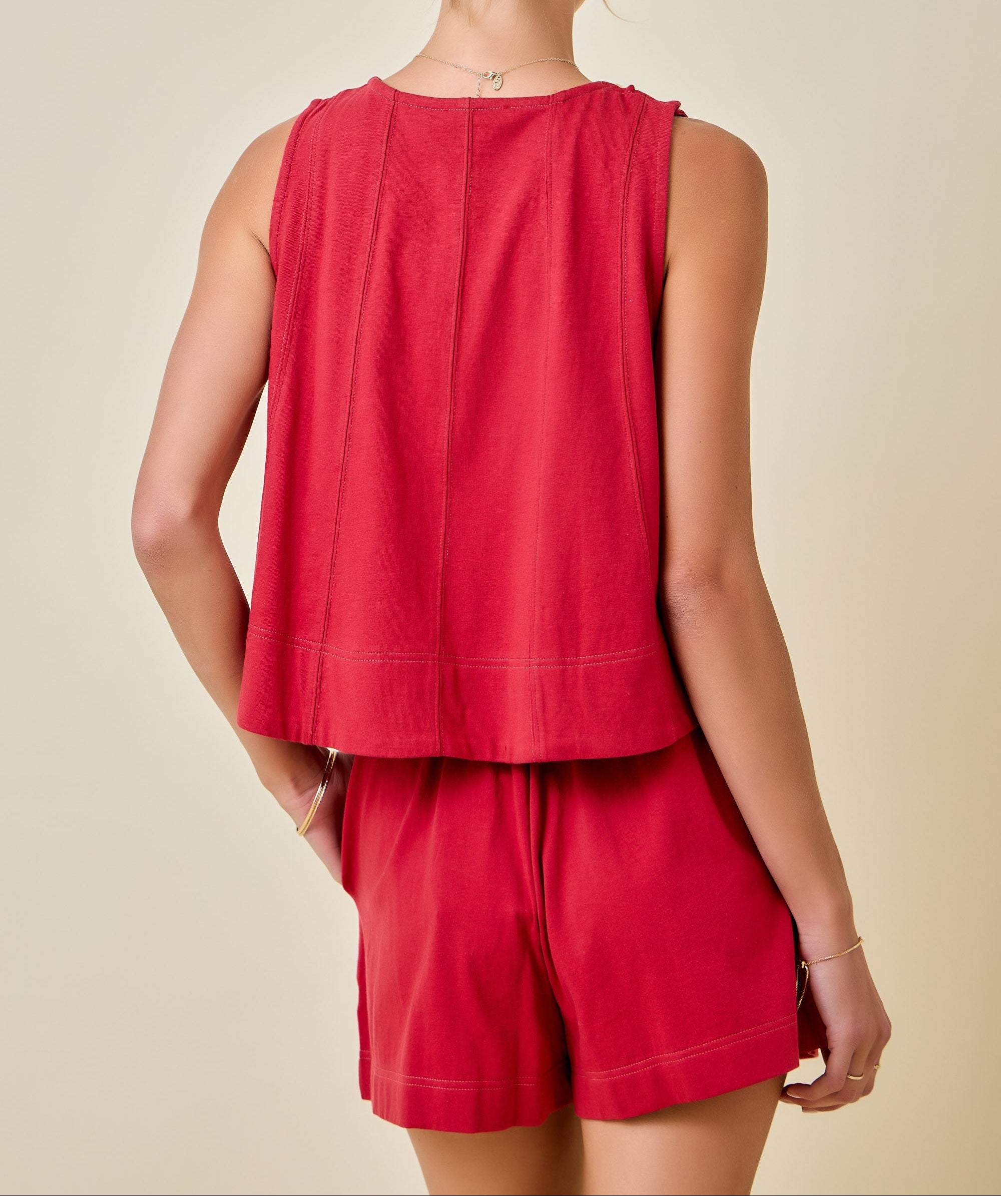 A woman shown from the back wearing a sleeveless red top and matching red shorts against a plain beige studio background.