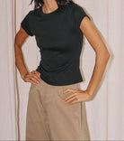 Woman wearing a black t-shirt and beige pants against a plain background