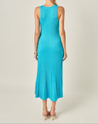 A woman viewed from the back wearing a sleeveless turquoise blue pleated midi dress against a light beige studio background.