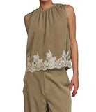 A model wearing a sleeveless olive green top with a white lace hem and matching olive green trousers, set against a solid black background.