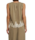 A woman viewed from behind wearing a sleeveless taupe top with a white lace hem and matching wide-leg trousers, set against a black background.