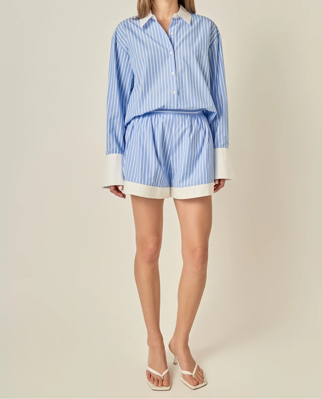 Woman wearing a blue and white striped shirt and shorts on a beige background