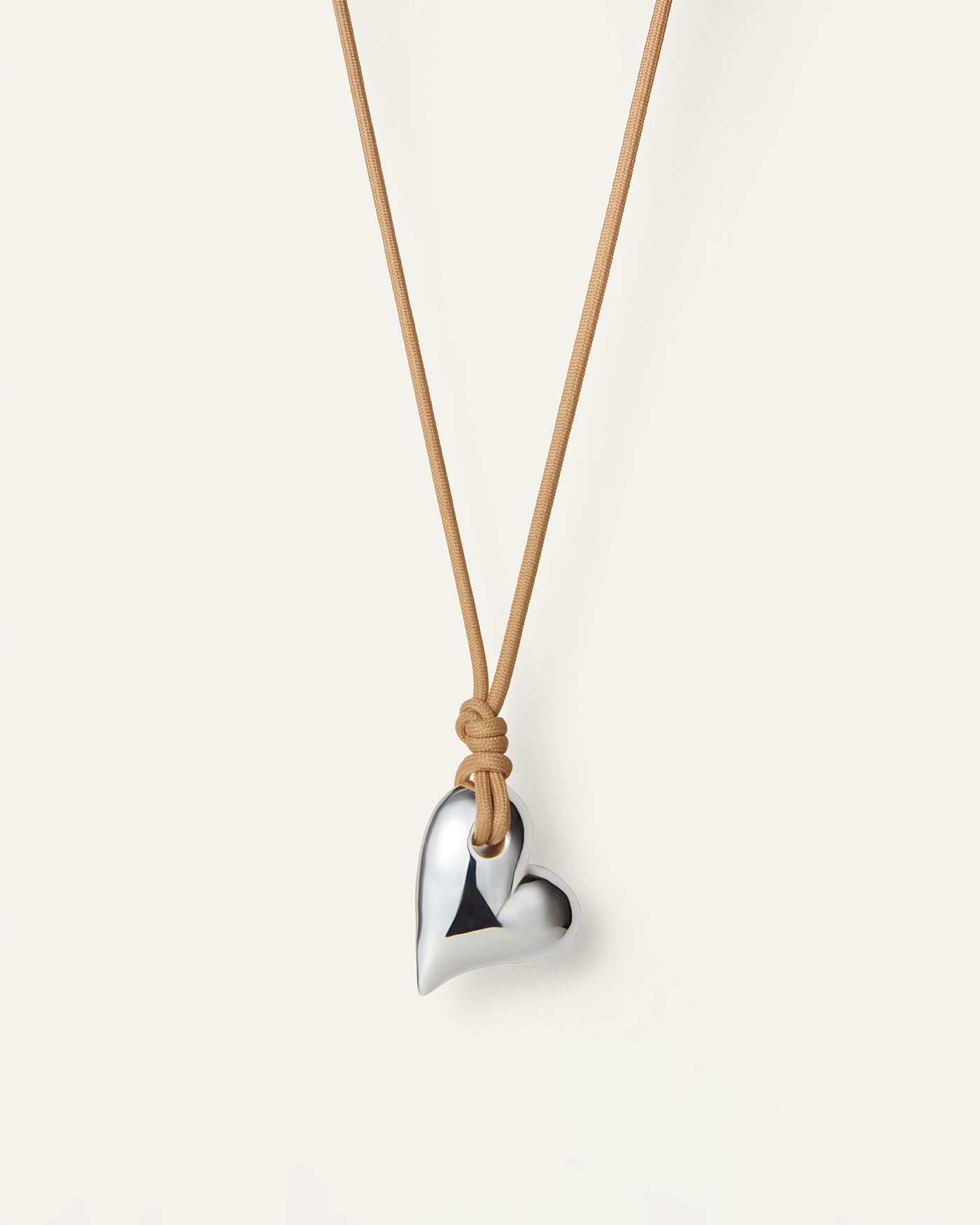A silver heart-shaped pendant on a beige recycled polyester cord necklace with a knot closure.