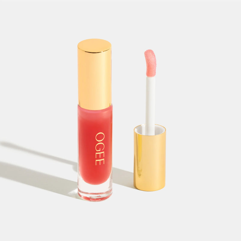 Lip gloss with gold cap and clear container on a light gray background