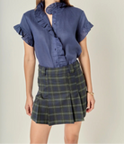 Woman wearing a blue blouse with ruffled details and a plaid skirt on a plain background