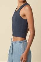 Woman wearing a dark blue tank top and light blue jeans against a beige background
