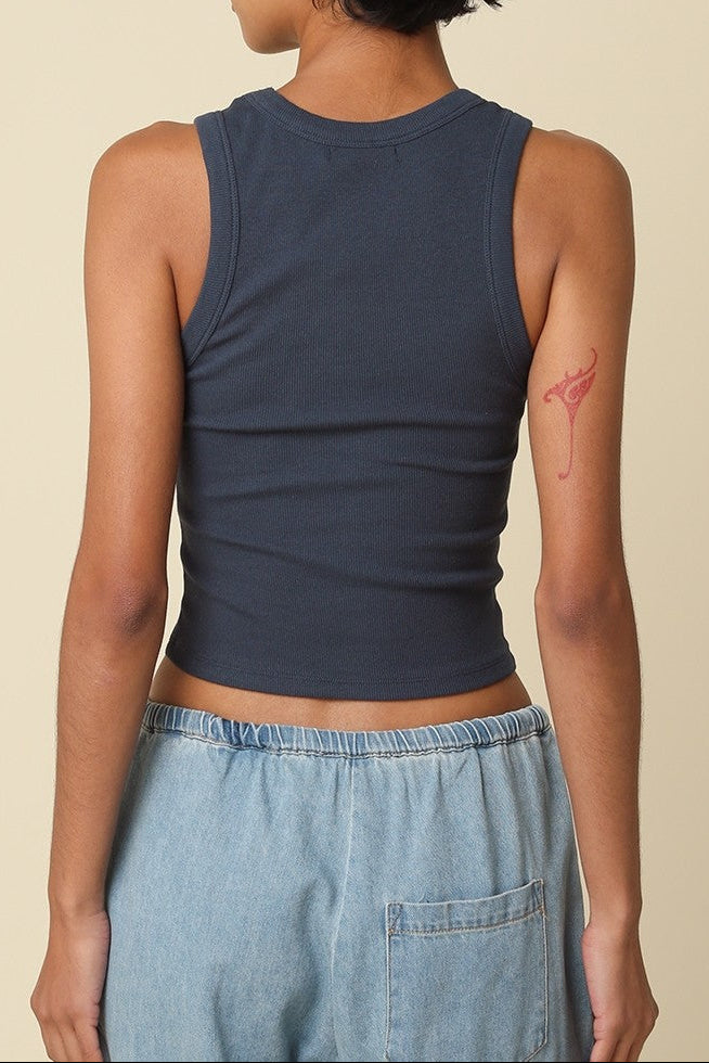 Person wearing a navy tank top and light blue jeans with a beige background