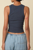 Person wearing a navy tank top and light blue jeans with a beige background