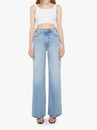 Woman wearing a white sleeveless top and light blue jeans on a white background