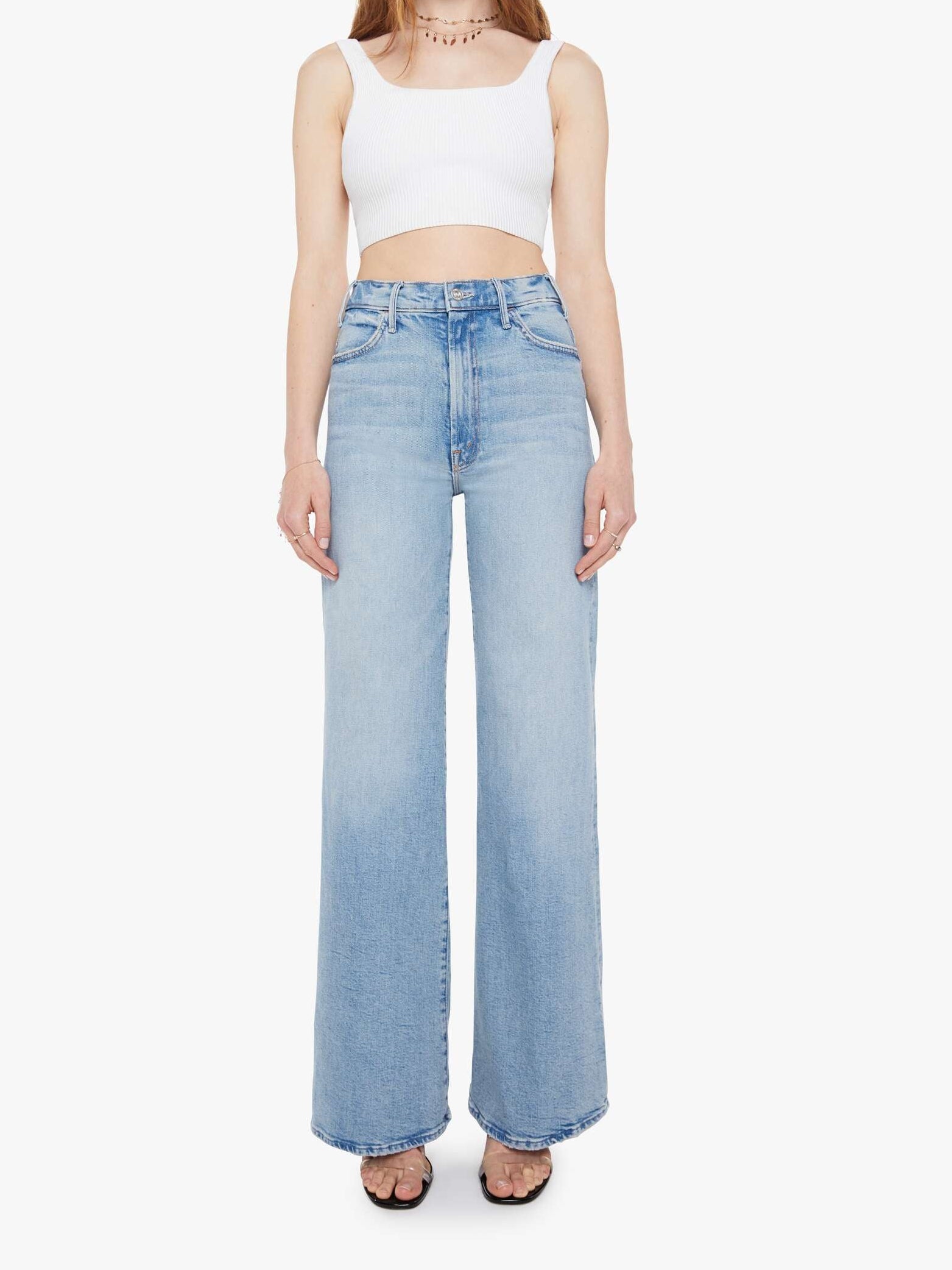 Woman wearing a white sleeveless top and light blue jeans on a white background